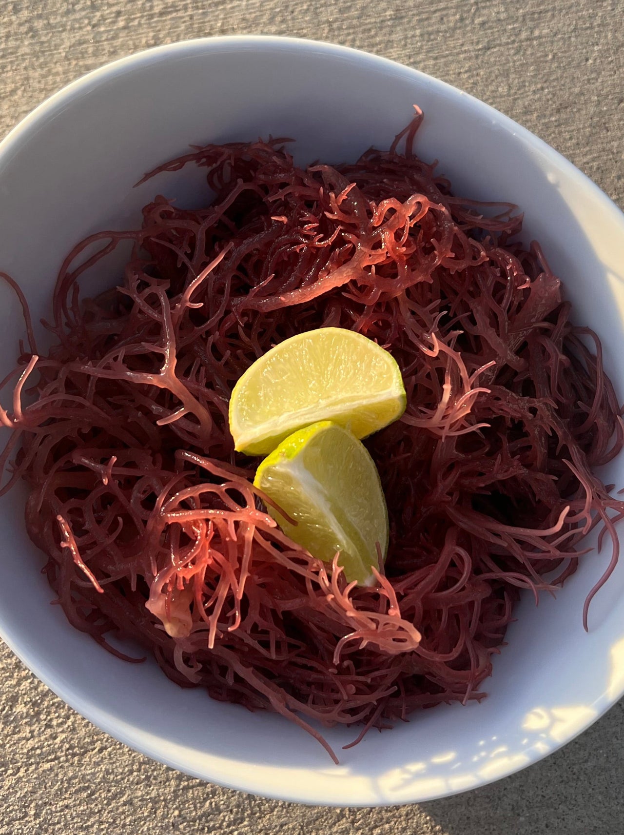 White bowl with purple sea moss and key lime wedges on a concrete surface
